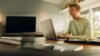 Mann mit Brille und Headset sitzt am Schreibtisch und arbeitet konzentriert an seinem Laptop in einem hellen, modern eingerichteten Raum.