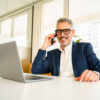Mann sitzt am Laptop und telefoniert