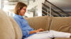 Frau die auf Sofa sitzt und am Laptop arbeitet