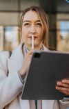 Frau hat ein Ipad in der Hand und hält ihren Stift nachdenklich an ihre Lippe