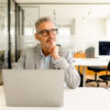 Mann der am Schreibtisch sitzt, in die Ferne schaut und über Wechsel seiner Maklersoftware nachdenkt