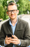 Mann mit Handy in der Hand der in die Kamera lächelt