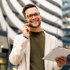Mann mit Tablet in der Hand und Smartphone am Ohr, lachend